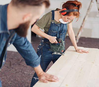 Ein junges Paar beim Verlegen von Holzfußboden, es modernisiert mithilfe eines 100.000-Euro-Kredits. 
