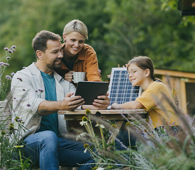 Eine Familie sitzt vor ihrer neuen Solaranlage am Gartentisch, die sie mit einem 100.000-Euro-Kredit finanziert hat.