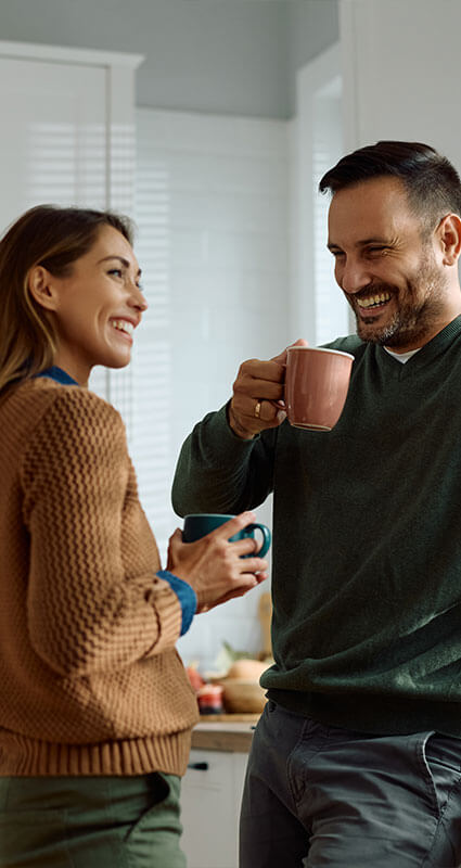 Ein Mann und eine Frau mit Kaffeetassen in der Hand strahlen: Ihr 100.000-Euro-Kredit wurde bewilligt.