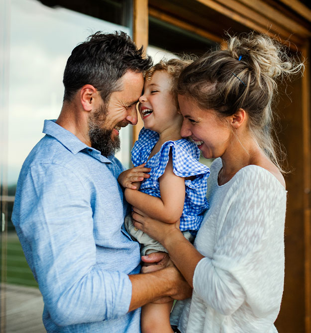 Eltern und Kind stehen lachend vor ihrem Haus, das sie mit einem 200.000-Euro-Kredit finanziert haben.