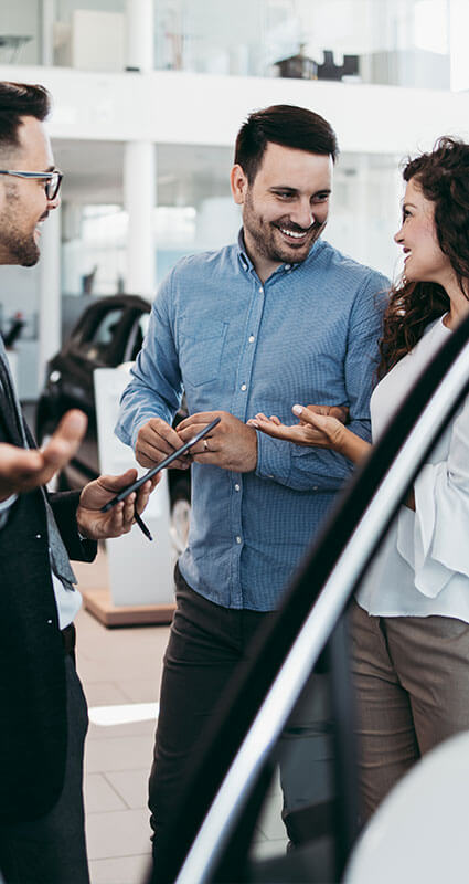 Ein strahlendes Pärchen unterschreibt sieht sich ihr neues Auto an