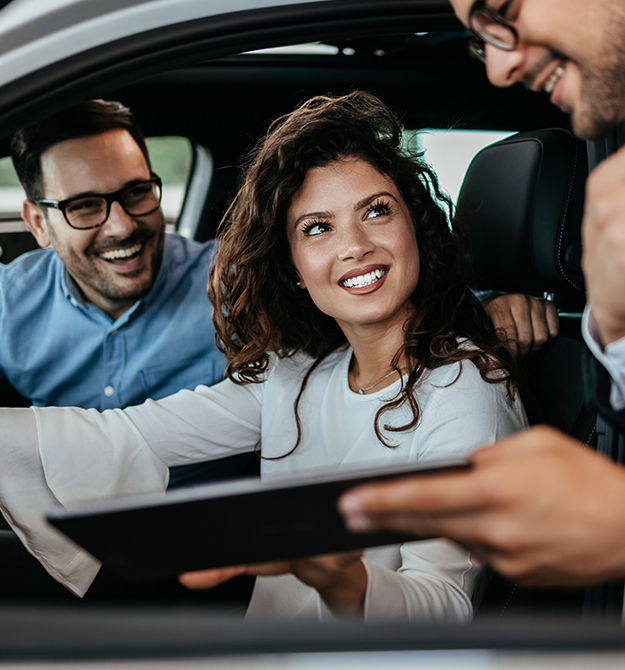Mann und Frau im Auto sprechen mit ihrem Berater freudestrahlend über einen Autokredit.