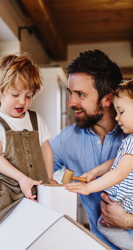 Ein Mann baut mit 2 Kindern ein Modellhaus.