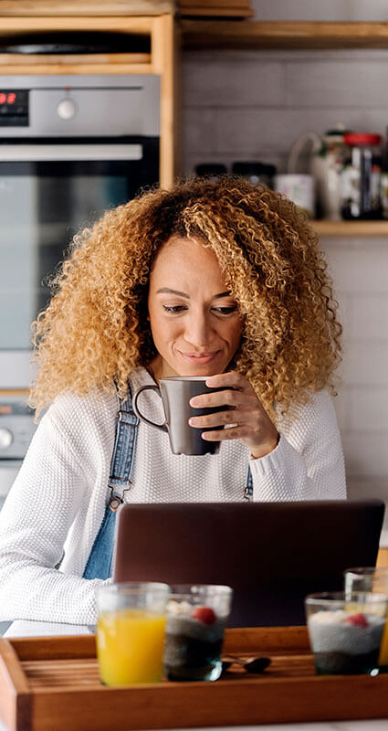 Ein Darlehen ist unter anderem für die Finanzierung von Küchenmöbeln geeignet. Ein Frau mit Kaffeetasse sucht in ihrem Laptop nach günstigen Darlehen.