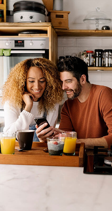 Auch auf dem Handy kann man ein Angebot für ein Darlehen einholen. Eine Frau und ein Mann suchen auf dem Smartphone nach einem geeigneten Darlehen.