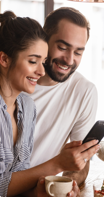 Mann und Frau stehen zusammen in der Küche und schauen lächelnd auf ein Smartphone
