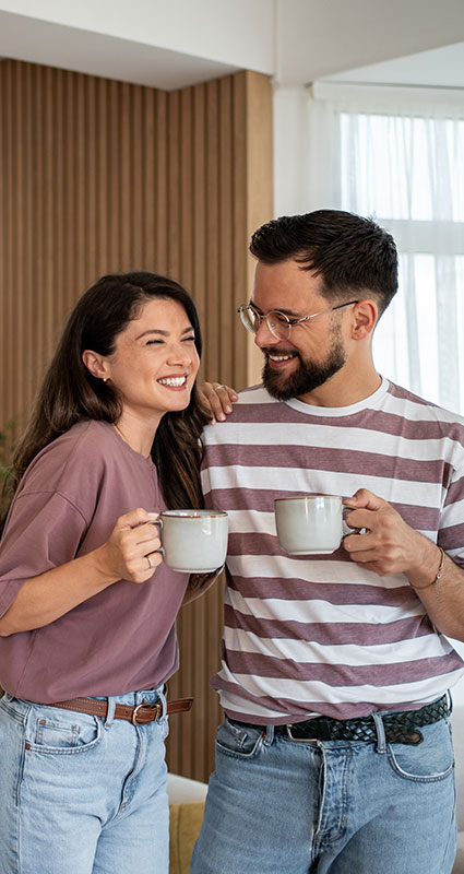 Zwei junge Leute mit Tassen in der Hand freuen sich über die günstigen Zinsen für Ihren 50.000-Euro-Kredit.
