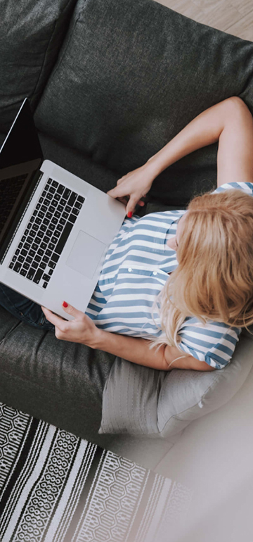 Frau hat Laptop auf ihrem Schoß, während sie bequem auf dem Sofa sitzt