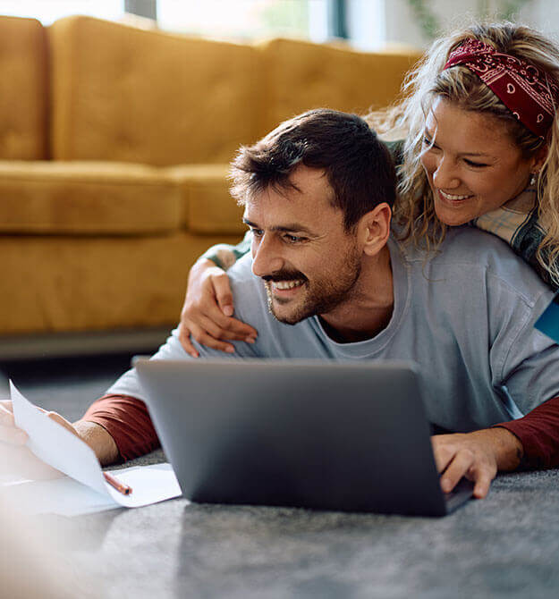 Ein lachendes Paar freut sich am Laptop über seinen Immobilienkredit.