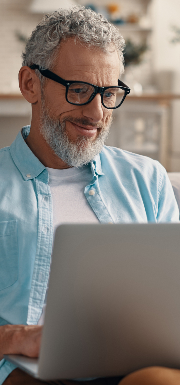 Ein Mann mit Brille freut sich am Laptop darüber, dass er seine Immobilie beleihen konnte.