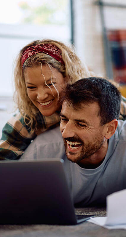 Ein fröhliches Paar schaut sich am Notebook seinen Immobilienkredit an.
