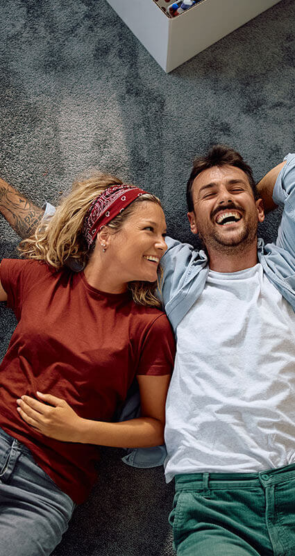 Ein Paar liegt lachend auf dem Boden seines mit Immobilienkredit finanzierten Hauses.