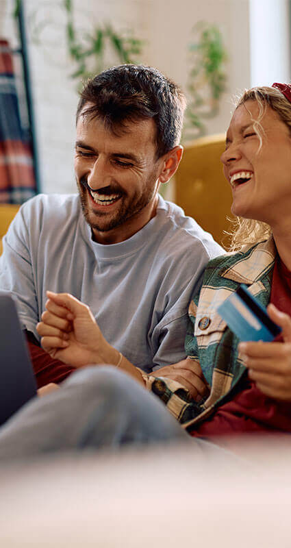 Zwei Menschen auf dem Sofa lachen, ihr Immobilienkredit ist genehmigt.