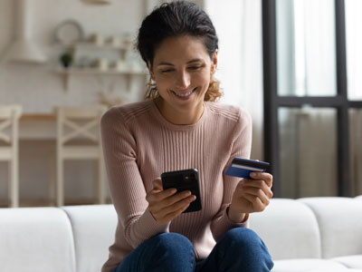 Eine Frau sitzt auf einem Sofa mit Kreditkarte und Handy in der Hand