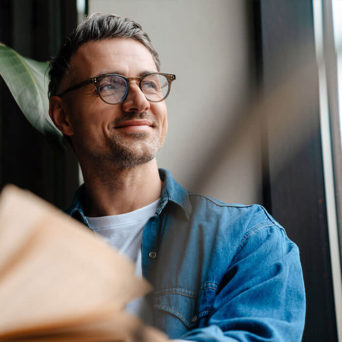 Ein Mann blickt entspannt aus dem Fenster und denkt über seinen Wunschkredit nach