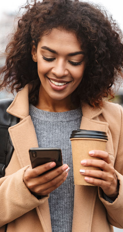 Eine Frau mit Kaffee in der Hand bekommt die Online-Zusage für ihren Privatkredit