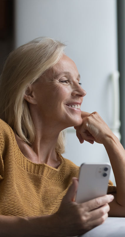 Eine Frau schaut glücklich aus dem Fenster und hält ein Handy in der Hand