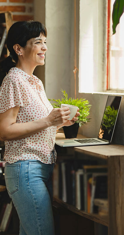 Was ist ein Nachrangdarlehen? Eine Person mit Kaffeetasse und Laptop lächelt, sie hat gerade ein Nachrangdarlehen aufgenommen.