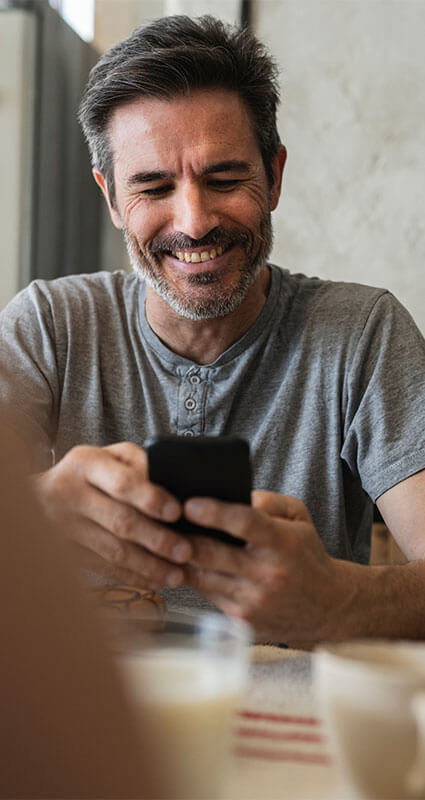 Möglichkeiten ein Nachrangdarlehen zu erhalten Mann schaut lächelnd auf sein Handy, um sich über ein mögliches Nachrangdarlehen zu informieren.