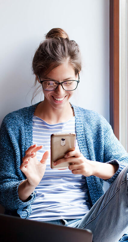 Sitzende Frau schaut lächelnd auf ihr Smartphone