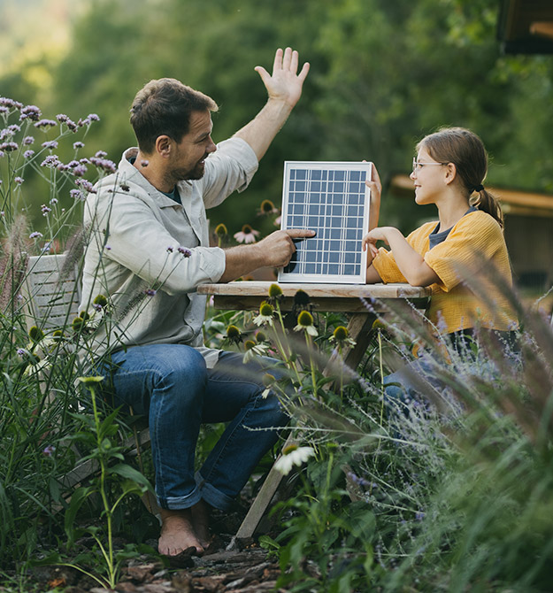 Ein Mann sitzt mit seiner Tochter im Garten und zeigt ihr eine PV-Anlage