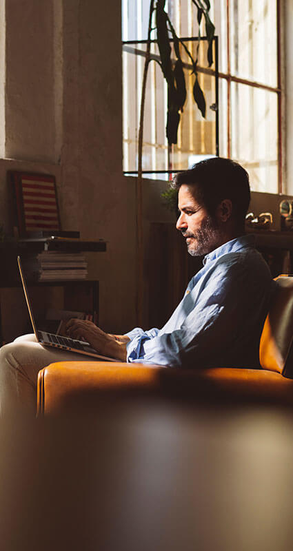 Rangrücktrittsvereinbarung im Falle einer Insolvenz der Kreditnehmenden Ein sitzender Mann informiert sich auf den auf seinem Schoß liegenden Laptop über die Rangrücktrittsvereinbarung