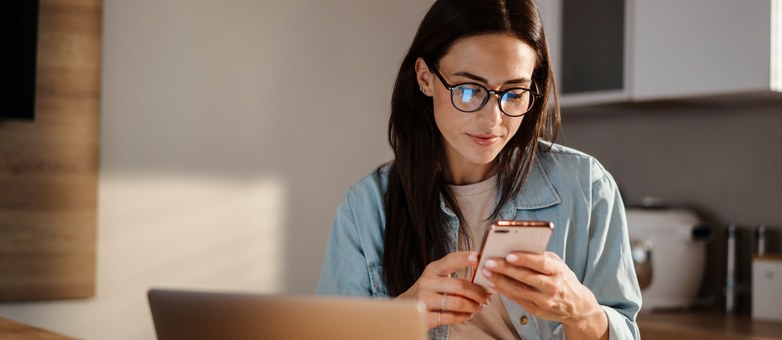 Eine Frau mit Brille prüft auf dem Smartphone ihre Bonität.
