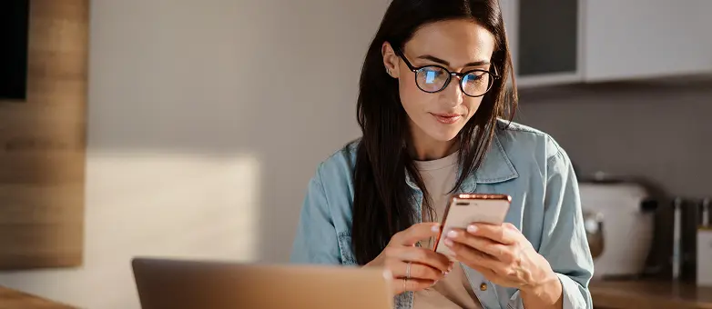 Eine Frau mit Brille prüft auf dem Smartphone ihre Bonität.