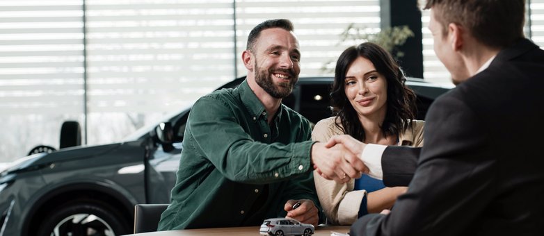 So funktioniert Leasing in der Praxis. Ein Paar bespricht im Autohaus das Thema Leasing und schüttelt dem Verkäufer die Hand.