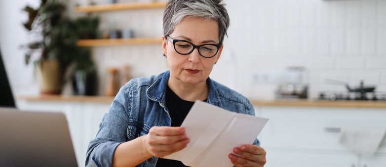 Unterlagen prüfen: So starten Sie in die Privatinsolvenz. Eine Frau mit Brille und grauem Haar liest am Küchentisch konzentriert ein Schreiben zur Privatinsolvenz.