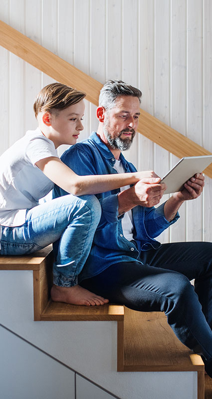 Mann und Sohn sitzen auf einer Treppe und schauen zusammen auf ein Tablet