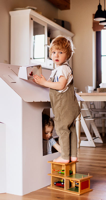 Zwei Kinder spielen gemeinsam an einer kleinen Indoor-Spielhütte zu Hause