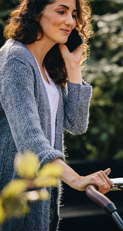 Frau lässt telefonisch über einen 20.000-Euro-Kredit beraten während sie einen Kinderwagen schiebt